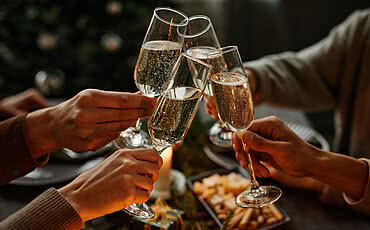 vier Personen beim Weihnachtsessen mit Champagner an einem eleganten Esstisch mit Kerzen sitzen